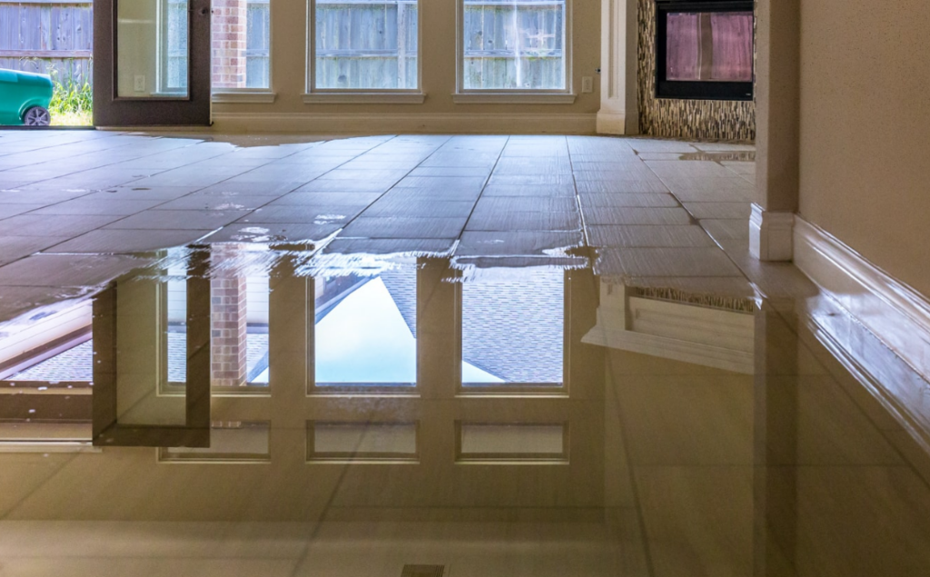 A flooded room featuring a fireplace and a window, with water covering the floor and reflecting light from outside.