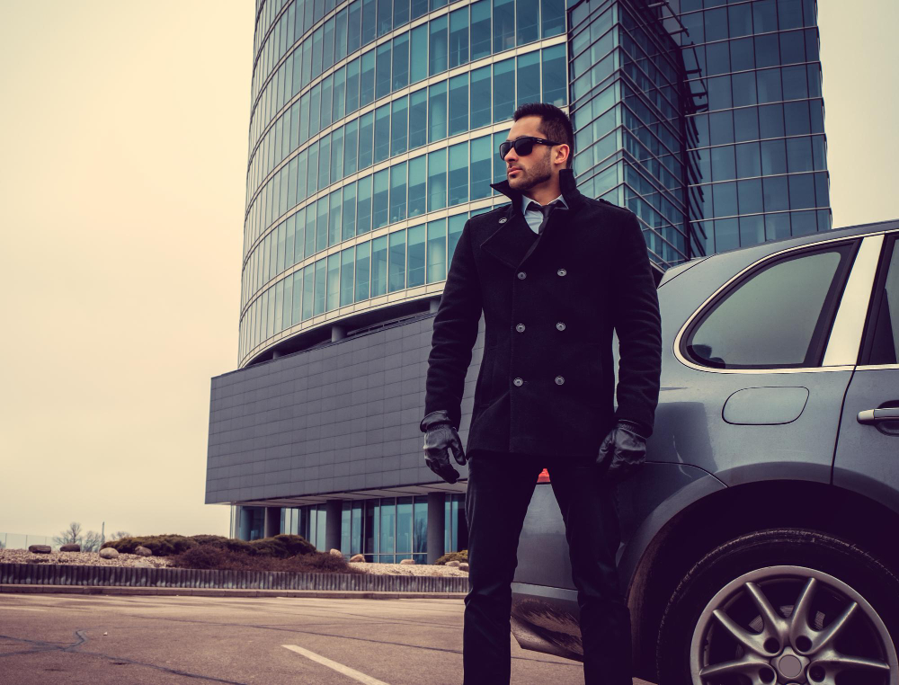 A security guard in a black coat and gloves stands beside a car, exuding professionalism and vigilance.