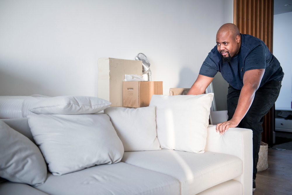 A man is relocating a couch in a tidy living room, showcasing professional clutter removal services in action.